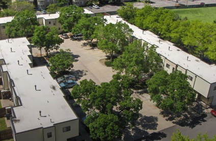 Aerial view of an apartment complex with white roofs and trees with green leaves