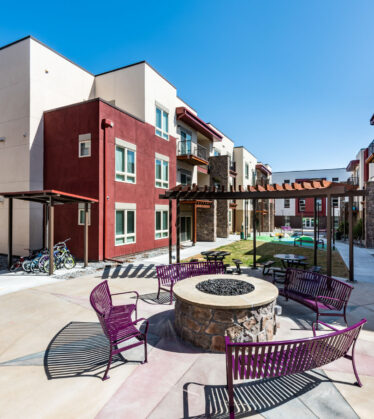 Courtyard with benches around a circular fire pit in front of white and dark red apartment buildings