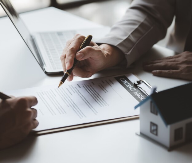 Hands of two people over a contract on a desk with one holding a pen