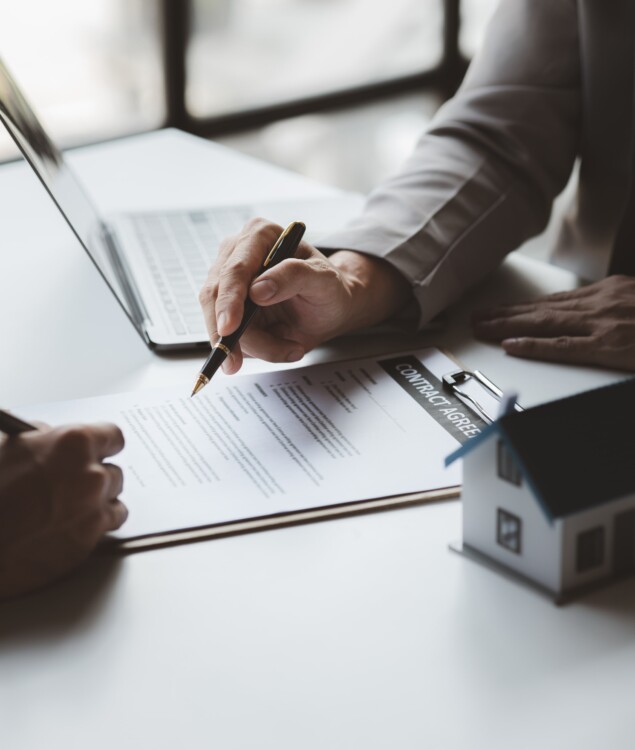 Hands of two people over a contract on a desk with one holding a pen